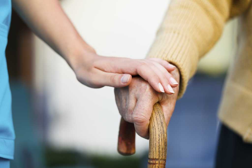 elderly person walking with cane embraced by caregiver