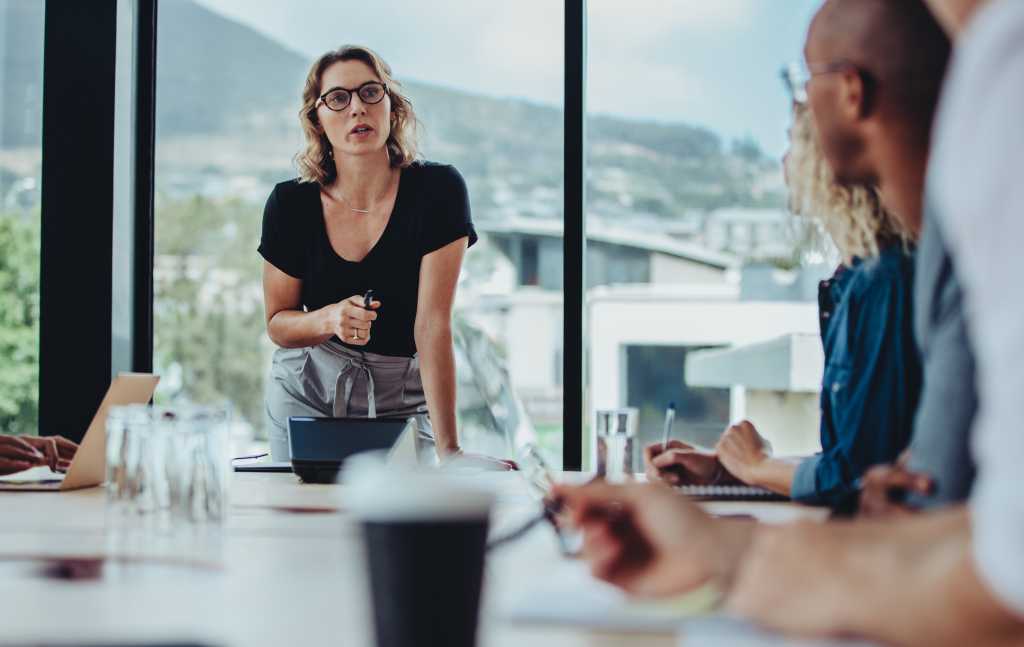 Businesswoman addressing a boardroom meeting with colleagues sitting at table. Female manager addressing her team at a meeting. Woman leadership