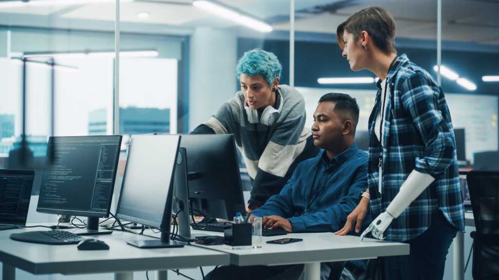 Team Meeting In Diverse Office: Project Manager with Disability points Prosthetic Arm at Computer Screen Talks with Multi-Ethnic Specialists. Software Engineers Collaborate on Creative Solution