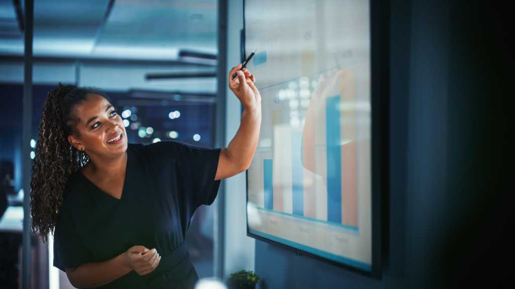 Company Operations Director Holds Sales Meeting Presentation for Employees and Executives. Creative Black Female Uses TV Screen with Growth Analysis, Charts, Ad Revenue. Work in Business Office.