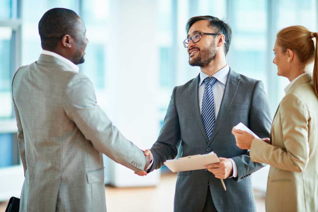 Two businessmen making agreement, their female colleague standing near by