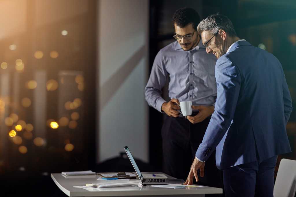 Businessman, colleagues and laptop at office in night for strategy, goals and target for investment in stock market. Stock broker team, reading and computer with innovation, working late and focus