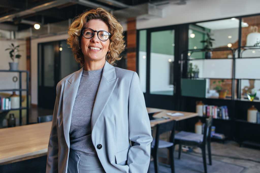 Portrait of a professional woman in a suit standing in a modern office. Mature business woman looking at the camera in a workplace meeting area.