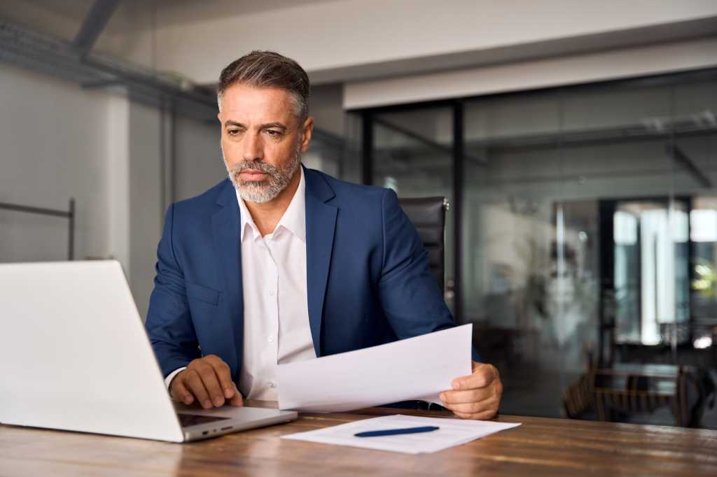 Middle-age Hispanic man using laptop computer for business studying, watch online financial webinar training meeting, video call. Focused mature Indian or Latin businessman work in office, copy space.