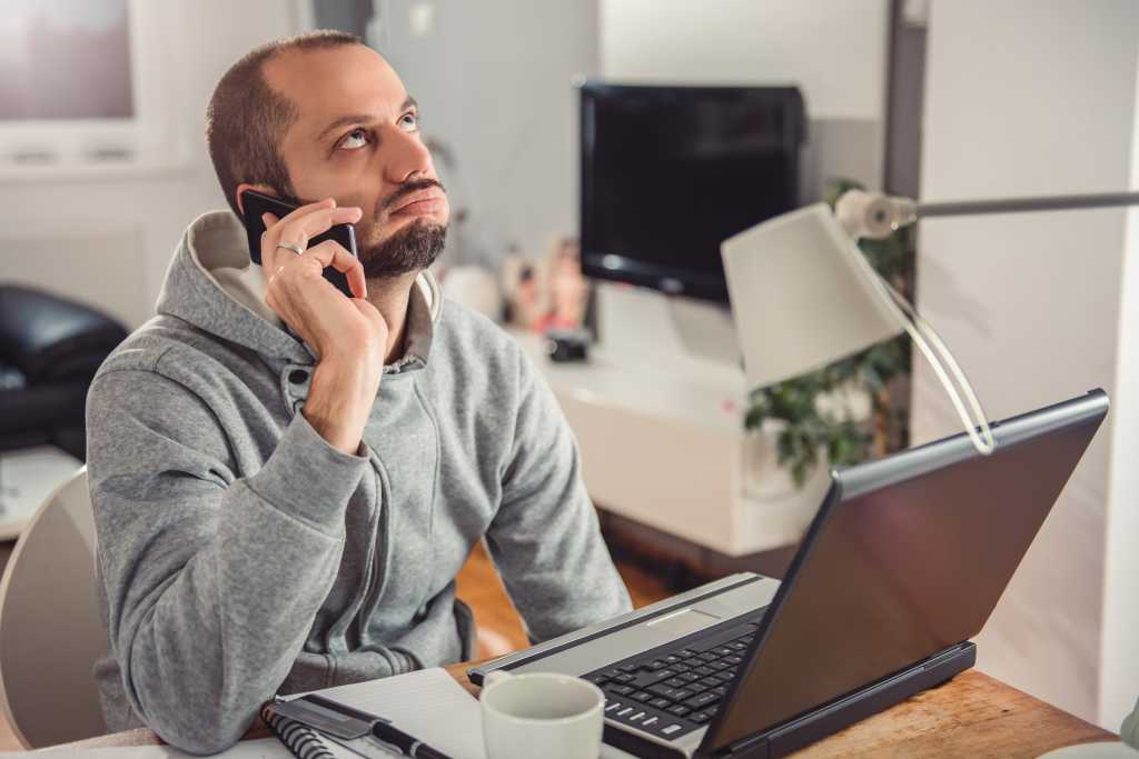 Frustrated man talking on smart phone at home office